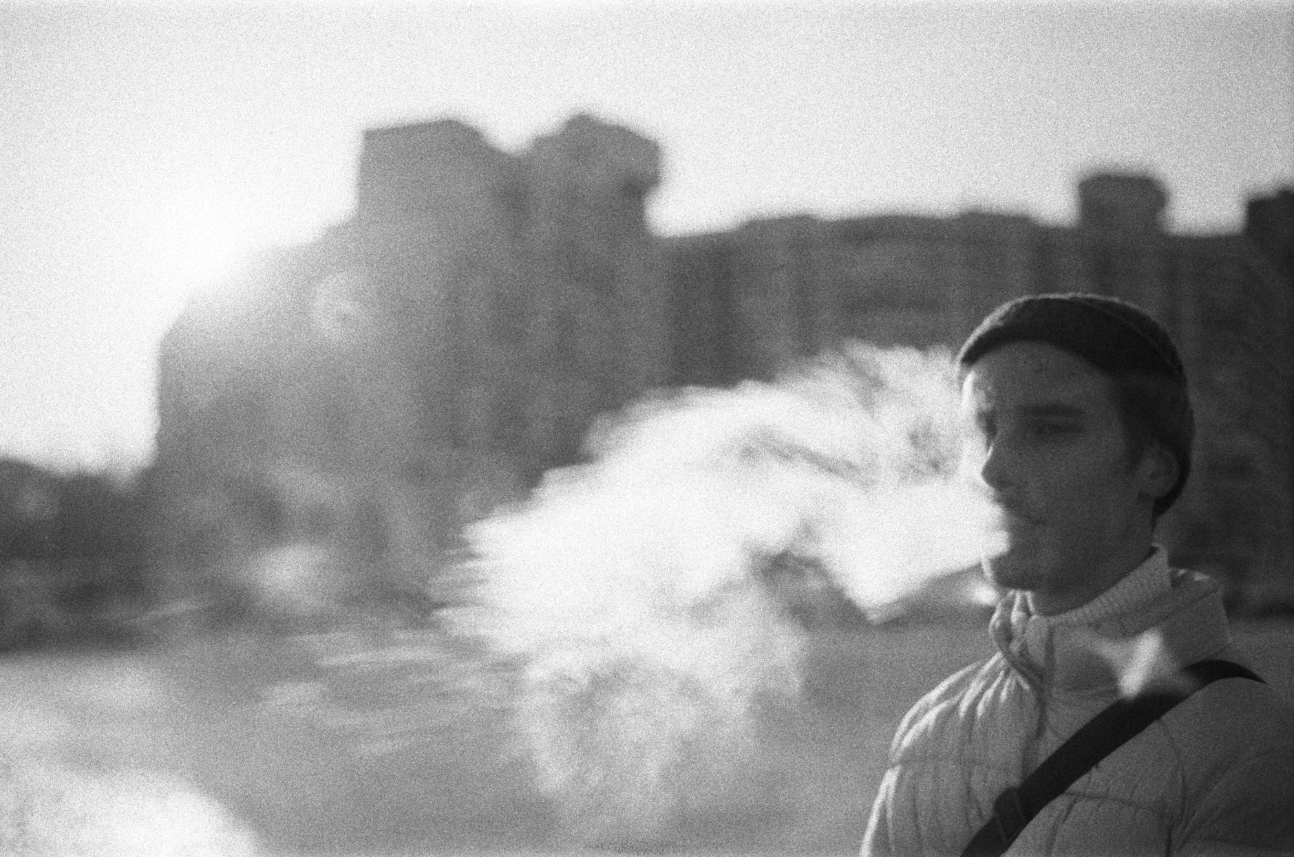 a grayscale of a man in winter clothing smoking